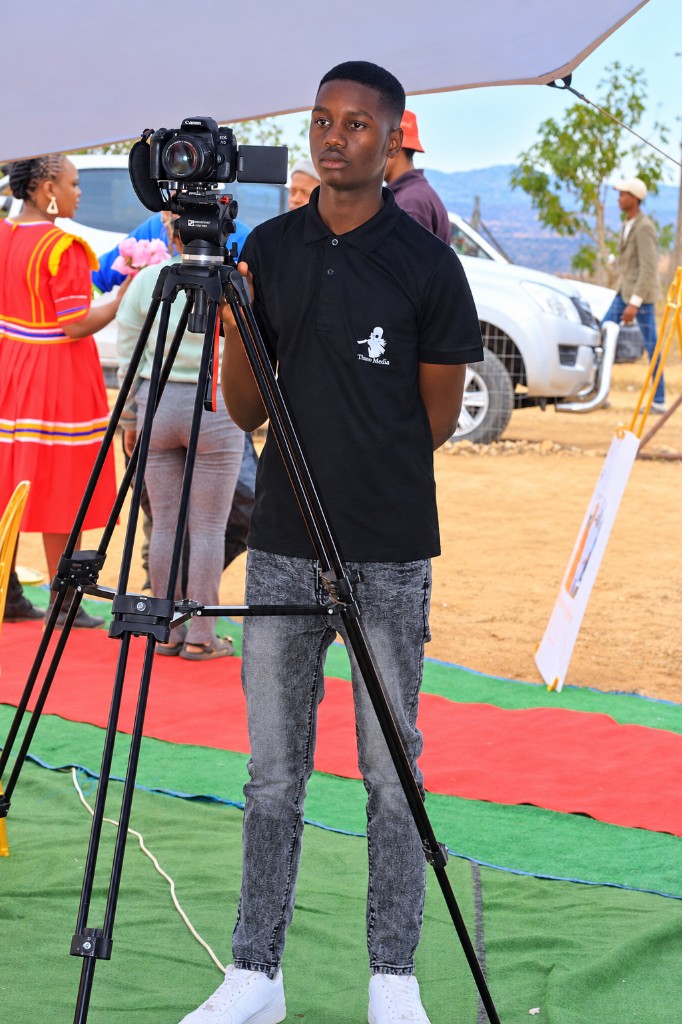The founder of Theo Media standing with a camera on a tripod at an outdoor celebration