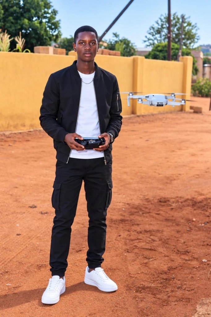 A photographer holding a drone controller, with a white drone hovering beside him