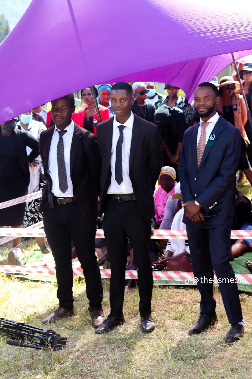 Three men in suits standing together under a purple tent