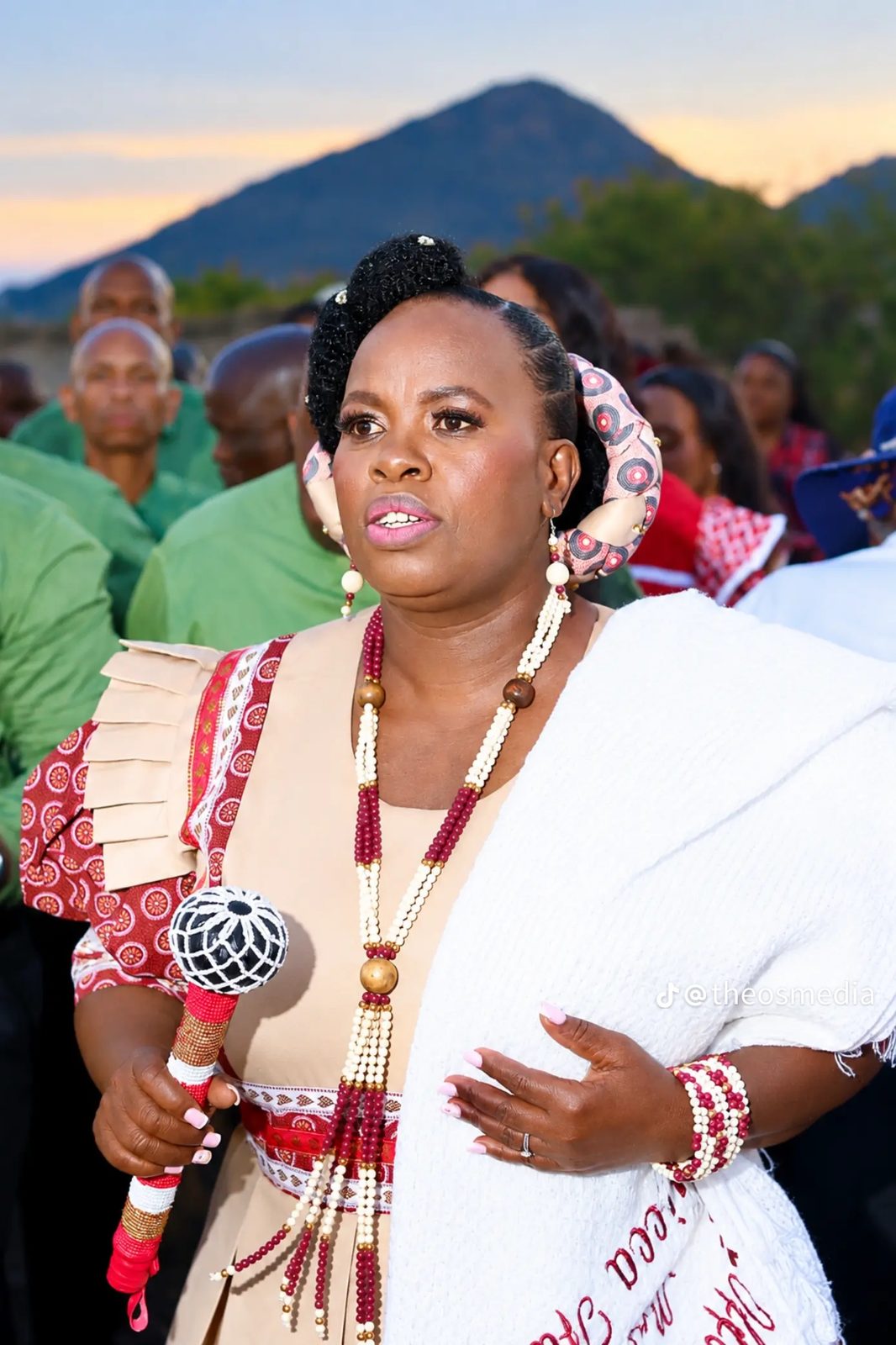 A woman in traditional dress holding a decorated microphone outdoors at dusk